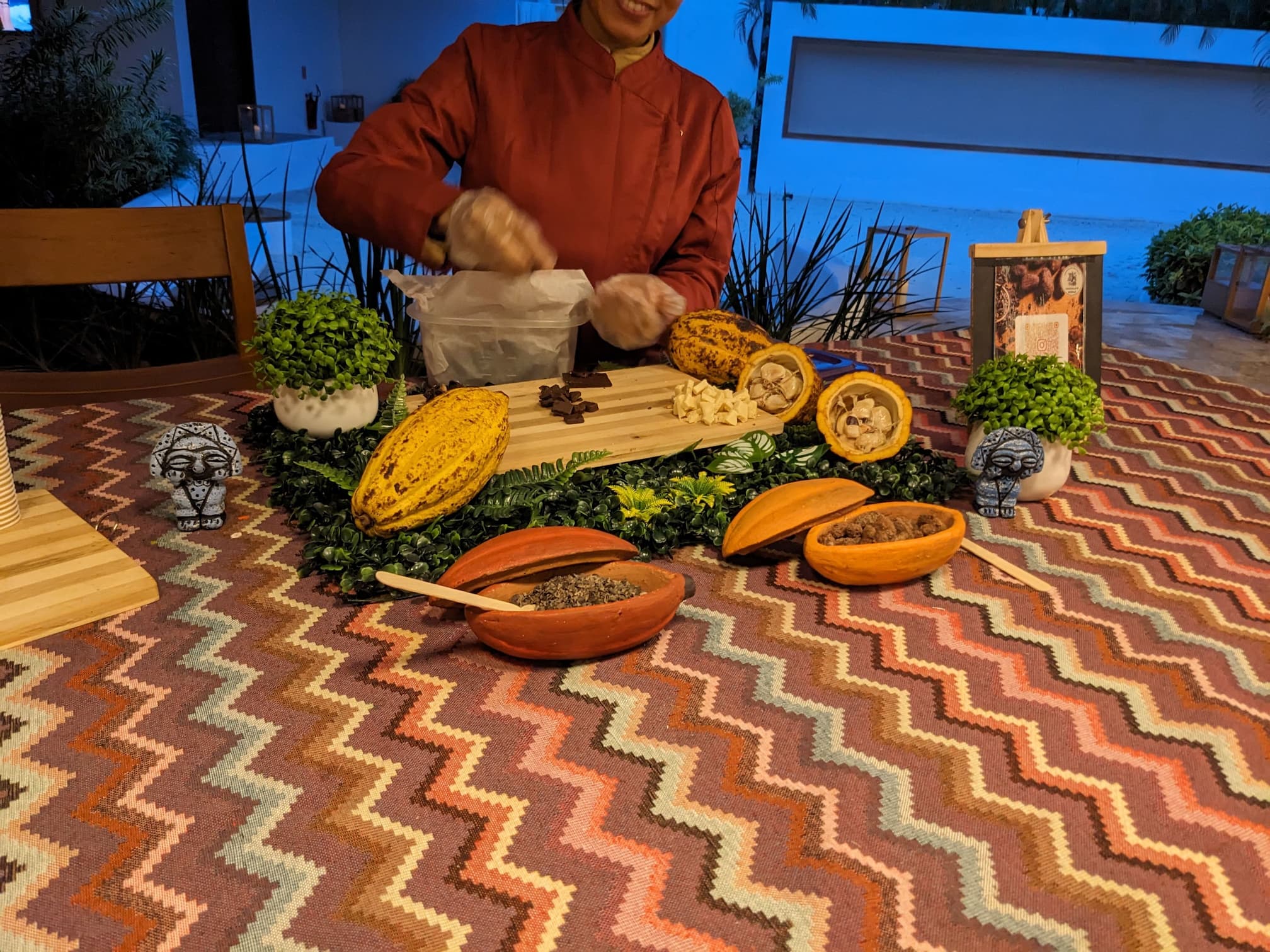 A tabletop with an ornate zig-zag tablecloth with an assortment of cacao in various stages of being processed.